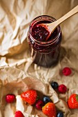 A jar of homemade raspberry jam on parchment paper with fresh berries