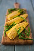 Breaded seabass fillets with a polenta and herb coating, served with samphire on a wooden board