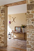 A wide entrance through a natural stone wall with a view of a wall table in a traditional hallway