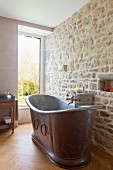 Vintage metal bathtub against stone wall in renovated bathroom with window