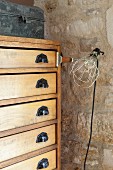 Chest of drawers with vintage handles and clip-on lamp against stone wall