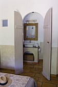 Blick auf gemauerten Waschtisch in Bad Ensuite durch die geöffneten Flügeltür, Bettende mit floral gemustertem Überwurf
