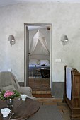 Vintage-style coffee cups on wooden table, armchair, récamier and view of double bed with mosquito net through open door