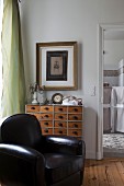 Black leather armchair and ornaments on vintage apothecary's cabinet below picture on wall
