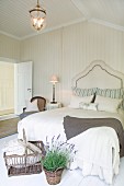 Korb und Lavendeltopf vor Doppelbett mit elegantem Kopfteil