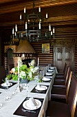 Wrought iron candle chandelier above set dining table and simple, leather-upholstered chairs in old dining room