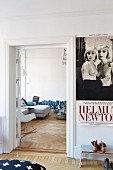 Vintage poster above shoe rack in bedroom with view of classic rocking chair and row of books in living room through open door