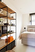 Retro shelving with black metal frame and wooden shelves in front of box-spring bed in bedroom
