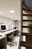 Arbeitszimmer mit langem Schreibtisch an Wand und Bürostühle im Klassikerstil, abgehängte Decke mit integrierter Beleuchtung, seitlich Treppenaufgang