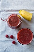 A banana and raspberry smoothie in a glass and in a jug