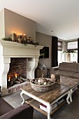 Rustic coffee table with curved legs in front of open fire below Christmas arrangement with lit candles on mantelpiece