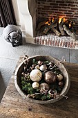 Weihnachtsdeko in Holzschale auf rustikalem Tisch, im Hintergrund offenes Kaminfeuer, seitlich Tierfigur auf Boden