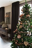 Decorated Christmas tree in room with brown floor-length curtains on windows