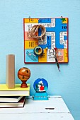 Retro board game used as pin board with gaming pieces used as hooks for scissors, twine and sticky tape above stacked books on desk
