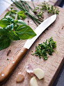 Basil, garlic and chives on a chopping board with a knife