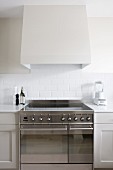 Detail of kitchen counter with modern stainless steel cooker with induction hob below white-clad extractor hood