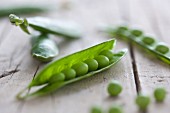 Fresh pea pods, some opened, on a wooden surface