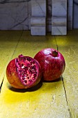 Pomegranates, whole and half, on a rustic yellow wooden surface
