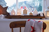 Avents decorations – house lanterns and wooden house on a driftwood board on a window sill