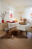 A country-style living room decorated for Christmas with red stars in the windows, a white two piece suite and an upholstered coffee table