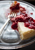 A slice of cheesecake with raspberry sauce with a bite taken out on a glass plate with a fork (close-up)