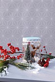 DIY Christmas arrangement of plastic animals and plastic fir tree in jam jar with artificial snow in front of branch of berries