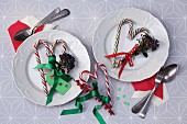 Zuckerstangen zu Herzform zusammengelegt, verziert mit Schleifenband und Beerenzweigen als weihnachtliche Tischdeko