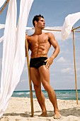 A sporty oung man posing by the sea wearing black swimming trunks