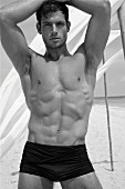 Sportlicher, junger Mann in schwarzer Badehose posiert am Meer
