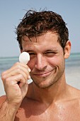 A young man with wet hair holding a seashell