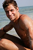 A young man by the sea with sand on his upper arm