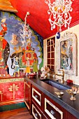 Indian-style mural on wall of traditional kitchen with ornate chandeliers with crystal pendants above kitchen counter