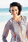 A dark-haired woman on a beach wearing a patterned blouse