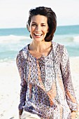 A dark-haired woman on a beach wearing a patterned blouse