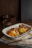 Baked apples with dried fruits in front of a jug of vanilla sauce