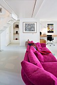Magenta couch in modern, open-plan interior with desk and classic chair in background