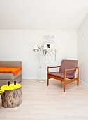 Wood-framed, fifties-style armchair next to standard lamp and tree stump table with surface painted yellow in foreground