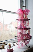 Toy figurines on vintage cake stand with pink lace ribbon on windowsill