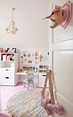 Offene Tür mit Spielzeug Trophäe dekoriert, Blick auf rundem Flickenteppich, rosafarbenen Dielenboden und weiße Kinderzimmermöbel