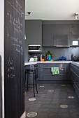 Blick in elegante graue Hochglanzküche mit einzelnen Musterbodenfliesen, Küchentheke und beschrifteter Tafelwand
