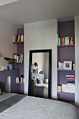 Angelehnter schwarz gerahmter Wandspiegel zwischen offenen mauvefarbenen Bücherregalen im Schlafzimmer