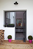 Elegant entrance area; box balls in pink pots flanking outside door and rustic stack of firewood on wooden terrace