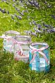 Three vintage-style glass tealight holders decorated with romantic floral patterns on lawn next to flowering lavender in garden