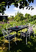 Wooden table and white chairs made from curved metal in summery garden