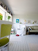 Chair with green upholstery, armchair in background and antique sofa against white wainscoting in cottage interior