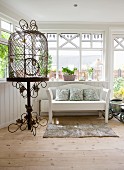Vintage bird cage on ornate metal stand and white bench in wood-clad conservatory