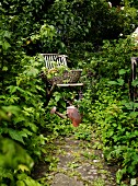 Korb auf Holz Klappstuhl und Vintage Giesskanne in dicht bewachsenem Garten