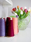 Colourful reels of thread with vase of tulips in blurred background