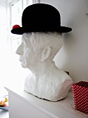 weiße männliche Gipsbüste mit schwarzem Hut dekoriert