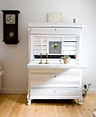 White-painted bureau with lit candles in brass candlesticks on folded-down desk in rustic interior